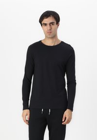 Camiseta negra de manga larga hecha de un tejido suave con un cuello redondo, diseño ajustado y un detalle de costura mínimo, combinada con pantalones negros.