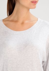 Hellgrauer Pullover mit Rundhalsausschnitt, gestrickter Textur und einem leicht entspannten Schnitt, der den weichen Stoff und das schlichte Design betont.