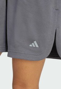 Pantaloni sportivi grigi realizzati in tessuto morbido, con un design a spacco laterale e un logo Adidas ricamato di un grigio chiaro sull'orlo.