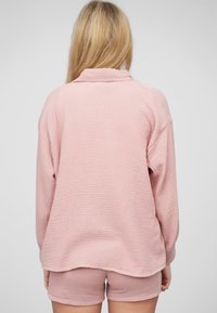 Top in tessuto texturizzato rosa chiaro con colletto e maniche lunghe, abbinato a pantaloni corti rosa coordinati, visto da dietro.