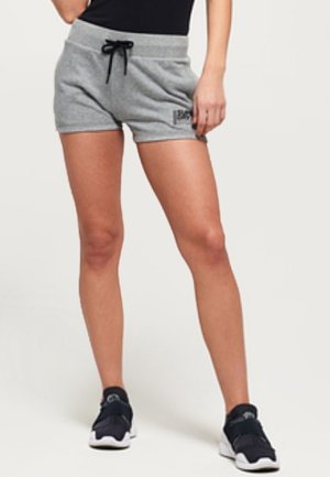 Femme portant un short de sport gris à cordon, un haut noir et des baskets noires, debout avec une main reposant sur la cuisse.