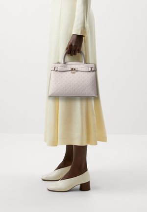 Borsa strutturata in pelle embossed rosa chiaro, con chiusura, doppio manico e superficie liscia. Indossata con un abito giallo fluente.