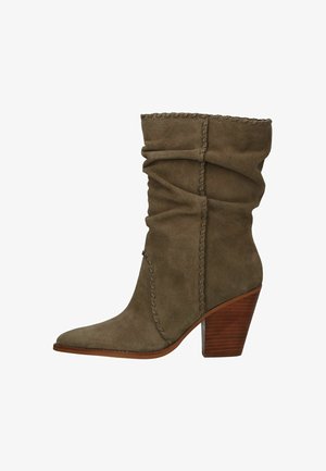 Botín de ante verde oliva con diseño holgado, punta puntiaguda y costuras decorativas; cuenta con un tacón grueso de madera.