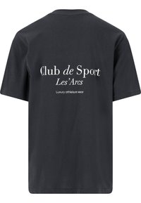 Mustat puuvillapaidat, joissa on lyhyet hihat. Takana valkoista tekstiä: "Club de Sport Les'Arcs" ja "Luxury athleisure wear."