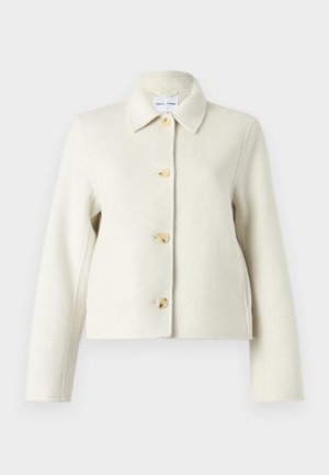 Κρεμ σακάκι από μείγμα μαλλιού με γιακά, τέσσερα μεγάλα ανοιχτόχρωμα κουμπιά και μακριά μανίκια. Λείο ύφασμα και κοντό σχέδιο.