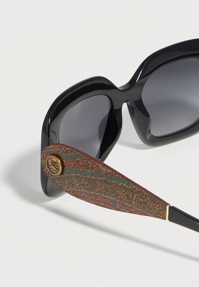 Lunettes de soleil noires oversize avec verres foncés et branches texturées multicolores à motifs, featuring un petit bouton logo rond.