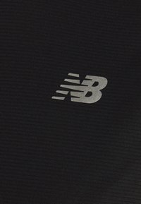 Černá sportovní tkanina s žebrovanou strukturou a reflexním šedým logem "NB" s pohybovými liniemi na jedné straně.