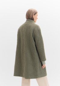 Grüner Fleece-Mantel mit einer strukturierten, weichen Oberfläche, ausgestattet mit einem hohen Kragen und langen Ärmeln mit Rippenbündchen. Mittellanges Design.