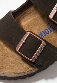 Sandalo in suede nero con due cinghie regolabili, fibbie in bronzo, plantare in sughero sagomato e suola in gomma texturizzata.