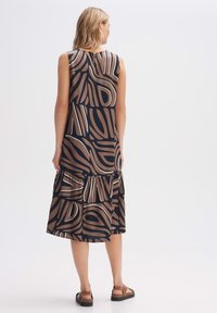 A sleeveless, tiered dress in a brown and navy pattern with abstract lines. Smooth fabric, round neck, and back button detail.