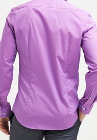 Koszula z długim rękawem w jasnofioletowym kolorze, o gładkiej fakturze, klasycznym kołnierzyku i mankietach zapinanych na guziki. Posiada zaokrąglony dół i dopasowany krój.