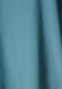 Un tissu texturé dans une couleur turquoise vibrante, présentant une surface lisse avec des variations subtiles dans le motif et la réflexion de la lumière.