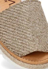 Sandalia deslizante de color beige tejido con punta abierta, detalles de yute en la suela y plantilla de cuero suave. Presenta un diseño de tira texturizada.