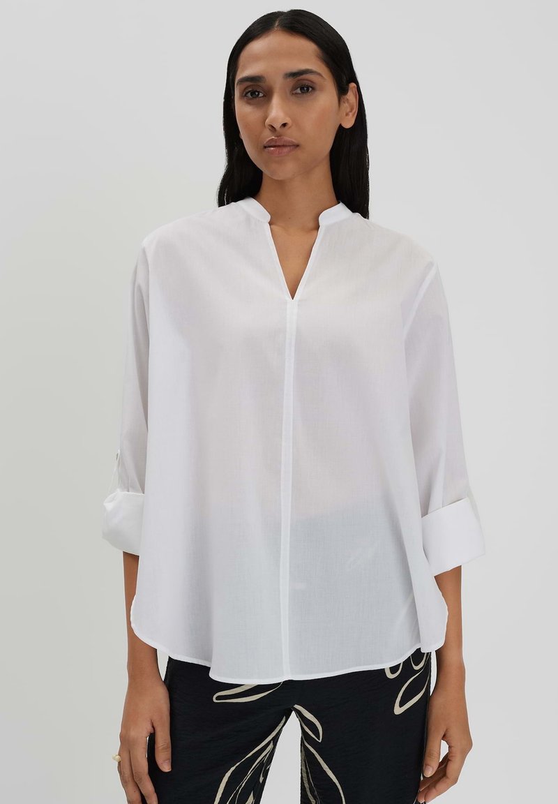 White long-sleeve blouse with a mandarin collar, featuring a front placket and rolled cuffs, made from lightweight fabric.