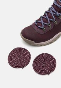 Bordowe wodoodporne buty trekkingowe z teksturowaną cholewką, metalowymi oczkami i niebieskimi sznurowadłami. Obok znajdują się dwa skręcone bordowe sznurowadła z różowymi akcentami.