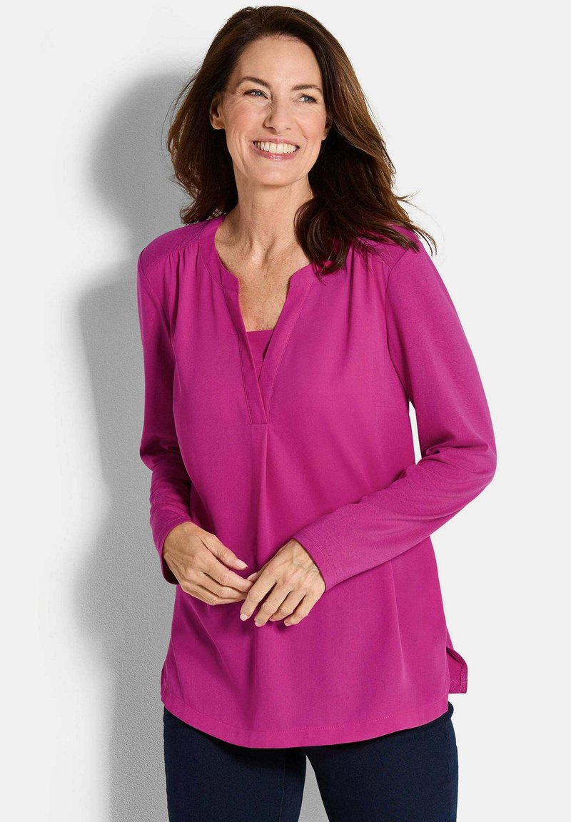 Blusa a maniche lunghe di un vivace rosa con scollatura a V, spacchi laterali e tessuto morbido e liscio. Vestibilità dritta con dettagli di cucitura minimi.