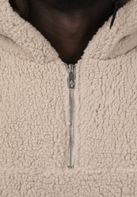 Beige fleece pullover with a high collar, featuring a silver double zipper and a textured, cozy exterior.