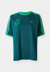 Žalioji medvilnės marškinėliai su žaliais akcentais, turintys apvalų kaklą, raglan stiliumi rankovėmis ir spaudintu Adidas logotipu ant krūtinės ir rankovės.