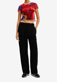 Punainen ja sininen abstrakti kuvioitu lyhyt toppi, jossa on röyhelöhelma, yhdistetty mustiin leveälahkeisiin cargo-housuihin, joissa on sivutaskut ja nappikiinnitys.