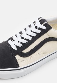 Schwarze und beige Wildleder-Sneaker mit weißen Schnürsenkeln, ausgestattet mit einem klassischen Wellenlogo und einer weißen Gummisohle. Strukturierten Oberfläche und Nähdetails.