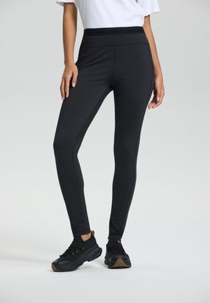 Zwarte legging met een brede, textuurband, een gladde stofafwerking, een aansluitend ontwerp en taps toelopende benen. Gecombineerd met zwarte sportschoenen.