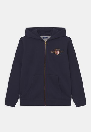 Marineblauwe hoodie met ritssluiting gemaakt van een katoenmengsel, met een gouden rits en een logo met rode en witte strepen op de borst. Twee steekzakken aan de voorkant.