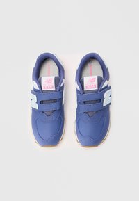 Une paire de baskets New Balance 574 bleues avec des accents blancs, des sangles Velcro et des semelles en gomme sur un fond blanc.