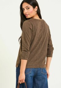 Brown, long-sleeve top with a round neckline and back seam detail, paired with blue wide-leg jeans. The fabric has a soft, textured finish.