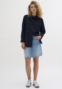 Navy button-up shirt with two chest pockets, paired with a light denim skirt featuring a frayed hem, and white sneakers with black accents.