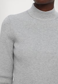 Maglione grigio chiaro a coste con colletto alto, dalla forma aderente e texture morbida, caratterizzato da sottili linee orizzontali.