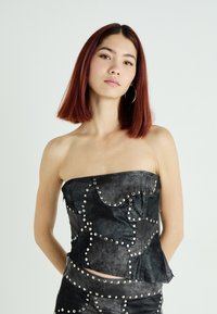 Top senza spalline in pelle nera con borchie metalliche, finitura testurizzata e design aderente con cuciture curve.