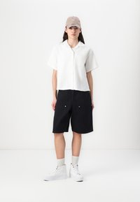 White short-sleeve button-up shirt, black knee-length shorts, and white high-top sneakers. The shirt has a single chest pocket.