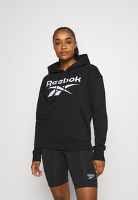 Czarna bluza z kapturem z przednią kieszenią typu kangur, z białym logo Reebok na piersi. Wykonana z miękkiego materiału o wygodnym kroju.