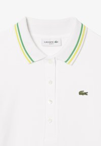Polo bianco slim fit, con colletto a costine a strisce verde e giallo, patta con tre bottoni e logo del coccodrillo ricamato.