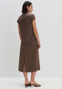 Bruine korte mouw top gemaakt van zachte stof, gecombineerd met een lange, bruine suède rok met een rugsplit. Bruine haksandalen maken de look compleet.