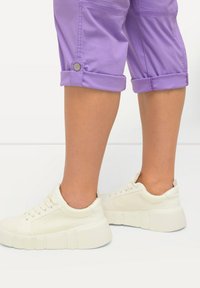 Pantalons courts violets avec ourlets roulés et détail de bouton, associés à des baskets blanches à semelle épaisse et au design minimaliste.