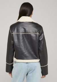 Giacca nera in pelle con colletto e rifiniture in montone bianco. Presenta un design corto e una vestibilità comoda, con una texture liscia.