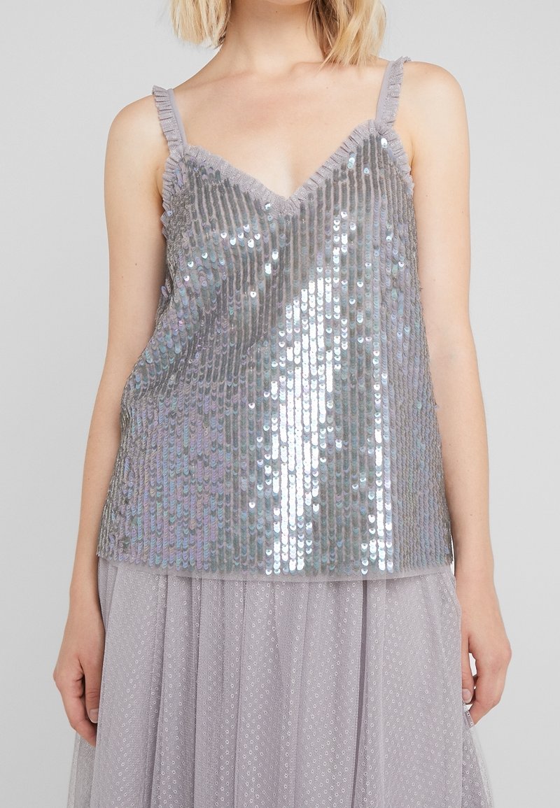 Camisola di paillettes argento con scollatura a V e spalline arricciate; presenta texture luccicanti e una vestibilità morbida, abbinata a una gonna in tulle grigio chiaro.