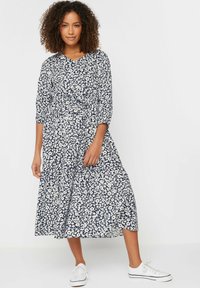 Vestido midi floral con base azul marino y patrón de flores blancas, que presenta un escote en V, mangas tres cuartos y una cintura ceñida.