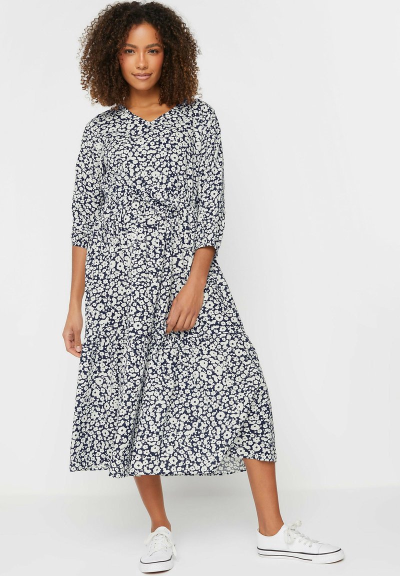 Vestido midi floral con base azul marino y patrón de flores blancas, que presenta un escote en V, mangas tres cuartos y una cintura ceñida.