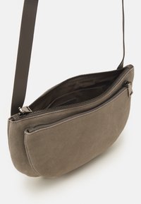 Piccola borsa a tracolla in camoscio color taupe con due scomparti con cerniera e tracolla scura regolabile, mostrata aperta su sfondo bianco.