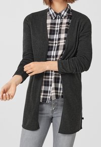 Tmavě šedý cardigan z měkkého materiálu, otevřený přední design, dlouhé rukávy, kombinovaný s černobílou kostkovanou košilí, neformální vzhled.