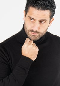 Pull en col roulé noir en matériau doux, avec un col haut et des manches ajustées. Design minimaliste sans motifs ni accents.