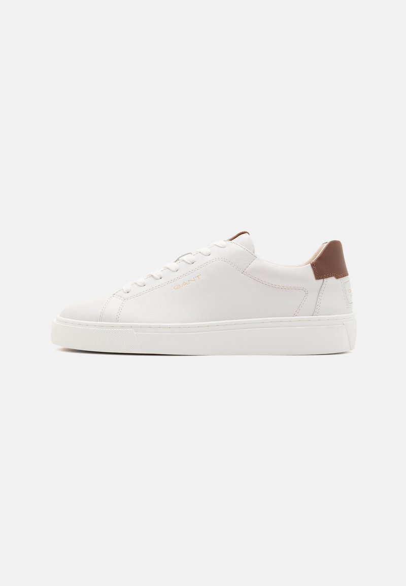 White leather sneaker with brown accent at the heel, round toe, flat white sole, and shoelaces, featuring a subtle logo.