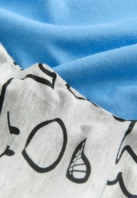Blå bomullstyg lager på lager med ljusgrått tyg som har svarta abstrakta mönster. Texturerna visar släta och något rynkiga ytor.