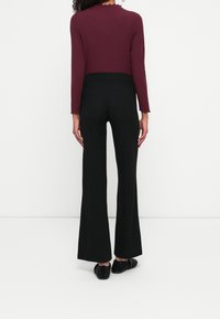 Bordeaux ribbat långärmad topp med scallopkanter, tillsammans med svarta vida byxor. Svarta texturerade slip-on skor fulländar outfiten.