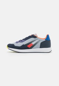 Sneakers con una parte superiore in mesh grigio, accenti blu navy, dettagli arancioni, lacci viola e una suola bianca testurizzata con punta gialla.