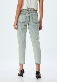 Vaaleansinisiä farkkuja, joissa on korkea vyötärö, suorat lahkeet ja viisi taskua. Kulunut pinta, jossa on näkyviä ompeluyksityiskohtia.