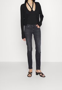 Cárdigan negro de canalé, camiseta de tirantes negra ajustada, jeans ajustados gris oscuro y sandalias de tacón negro con tiras. Diseño simple y estilizado.