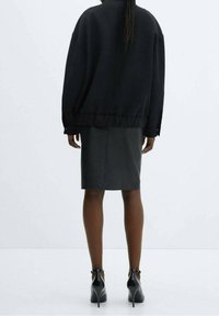 Sweat-shirt noir surdimensionné avec encolure arrondie, coupe ample et ourlet côtelé, associé à une jupe noire ajustée et des chaussures à talons hauts.